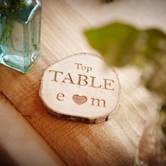 a wooden table topped with a vase filled with green leaves and a small plaque that says top table eom