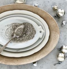 a white plate topped with silver glitter next to two bowls filled with silver spoons