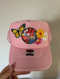 a pink hat with flowers and a butterfly on the front is held up by a woman's hand