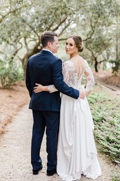 a bride and groom standing together in front of an oak tree lined path at their wedding