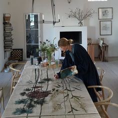 a woman is working on a table in a room with white walls and wood floors