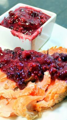 a white plate topped with meat covered in cranberry sauce next to a bowl of fruit