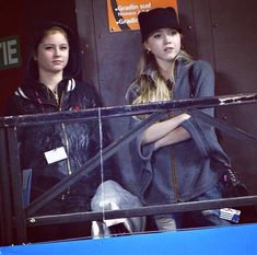 two young women are sitting on a balcony looking out at the street from behind them