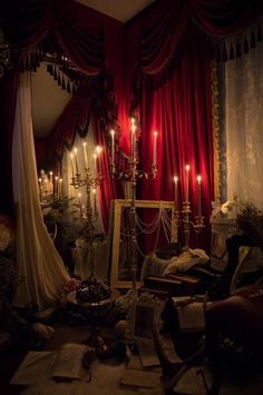 a room filled with lots of furniture and candles in the dark, surrounded by red drapes