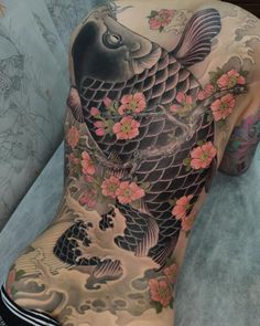 the back of a woman's body with tattoos on it and koi fish