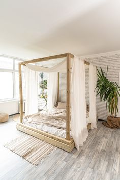 a bed with white sheets and curtains in a room next to a potted plant