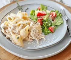 a plate with pasta and salad on it sitting on a wooden table next to a fork