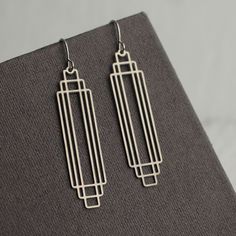 These great earrings are made with cut silver steel and feature a graduated rectangular art deco design.  They remind us of classic Deco architecture, like the Chrysler building!   The earrings measure 45mm (just under two inches) in length and have silver plated ear wires.   They have been designed and made in our Edinburgh studio.   This piece of handmade jewellery comes packaged in a nice recycled gift box with a handmade tag, all ready to give or keep. We also have these earrings in gold brass, as well as  many other Art Deco designs!  🖤 FASTER SHIPPING 🖤 Need this fast? We offer a Faster Shipping option here: https://www.etsy.com/uk/listing/100107311/faster-shipping-priority-post-upgrade 🖤 GIFT MESSAGE & WRAP SERVICE! 🖤 https://www.etsy.com/uk/listing/750160511/gift-wrap-wrapping- Art Deco Metal Drop Earrings, Art Deco Silver Metal Earrings, Silver Art Deco Pierced Earrings, Silver Sterling Silver Art Deco Earrings, Nickel-free Art Deco Metal Earrings, Gold Bra, Art Deco Jewelry Vintage, Earrings Aesthetic, Vintage Modern