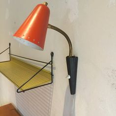 an orange lamp hanging from the side of a white wall next to a wooden table