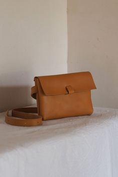 a tan leather purse sitting on top of a white tablecloth next to a brown strap