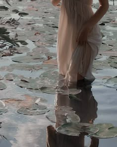 a woman standing in the water holding an umbrella over her head and wearing a pink dress