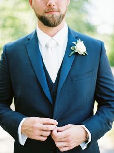 a man in a blue suit and white flower boutonniere is looking at the camera