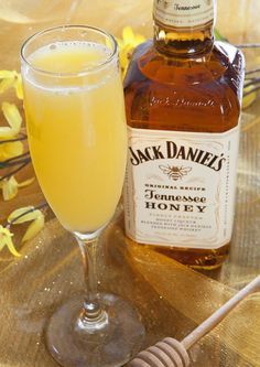 a bottle of jack daniels honey sits next to a glass filled with liquid and a honey stick