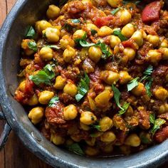 a bowl filled with chickpeas and tomato sauce on top of a wooden table