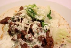 a taco filled with meat, cheese and lettuce on a white plate