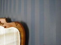 a bedroom with blue striped walls and a wooden bed frame in the corner, next to a window