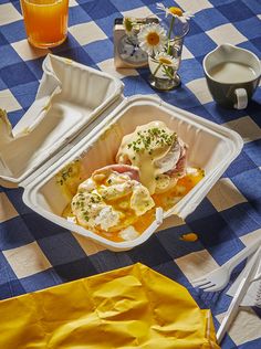 an open takeout container with eggs and ham in it on a checkered tablecloth