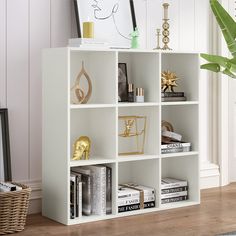 a white book shelf with books and other items on it next to a potted plant