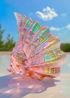 a pink glass shell sitting on top of a white table under a blue sky with clouds