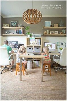 two children sitting at a desk in front of computer monitors and bookshelves with shelves above them