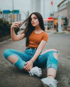 a young woman sitting on the ground with her hair blowing in the wind and wearing ripped jeans