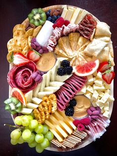 an assortment of cheeses, fruits and meats on a platter with grapes