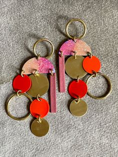 two pairs of earrings with different colors and shapes on them, one is pink, the other is red