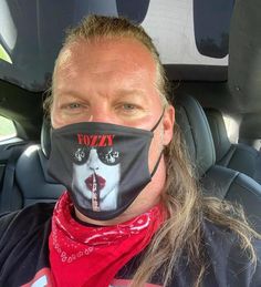 a man with long hair wearing a face mask in the back seat of a car