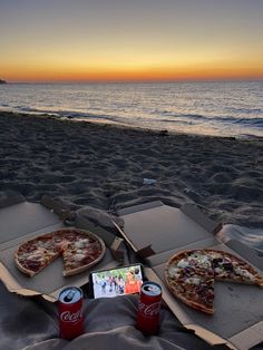 two pizzas and soda on the beach at sunset