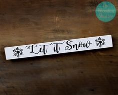 a sign that says let it snow on a wooden surface with the word'let it snow'in black and white