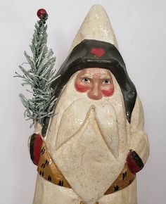 a ceramic santa clause holding a christmas tree in his hand and wearing a black hat