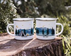 two camp mugs sitting on top of a tree stump