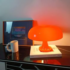 an orange lamp sitting on top of a table next to a white cup and mug