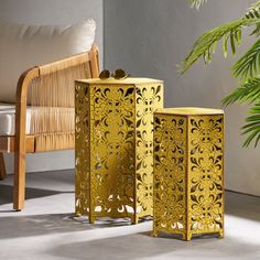 two golden vases sitting next to each other near a chair and potted plant