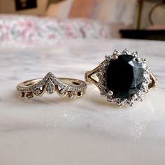 two engagement rings sitting on top of a white table next to each other, one with a black stone in the middle