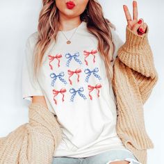 A cute ribbon shirt for all my Coquette Girlies. Coquette Clothing thats retro  for 4th of July, Vintage 4th of july Tee Soft and perfect for summer. A retro 4th of July Shirt, perfect as an outfit for our independence day. Merica fourth of July Tshirt Q U I C K * F A C T S * ♥️ 100% Soft cotton ♥️Design is high quality digital print ♥️ Wash and dry normally. Do not iron directly on the print. * S I Z I N G * ♥️ Sizing is unisex so runs like men's ♥️Most women find their typical size works best. Cute Holiday Tops For Spring, Cute Tops For Spring Holiday, Cute Spring Holiday Tops, Coquette Tshirt, Coquette Tshirts, Americana Style T-shirt With American Flag Print, Americana Style Cotton T-shirt With American Flag Print, White Americana T-shirt With American Flag Print, Ribbon Shirt