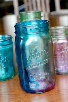 four mason jars are lined up on a table top, one is blue and the other is pink