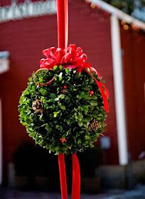 a christmas wreath hanging from a pole with red ribbon and bow on it's top