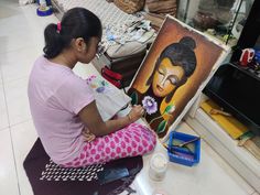 a woman sitting on the floor next to an easel with a painting in front of her