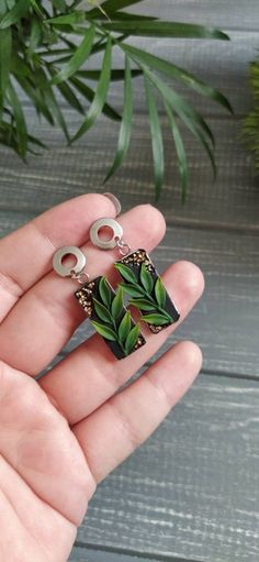 a person is holding some plants in their palm tree earrings, which are shaped like rectangles with leaves on them