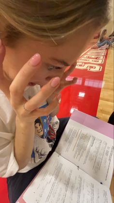 a woman holding her hand up to her face while looking at an open piece of paper