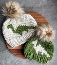 two knitted hats sitting on top of a wooden platter next to each other