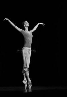 a woman is standing on one leg with her arms out in the air while wearing ballet shoes