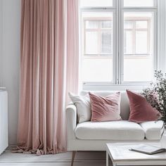 a living room with a couch, coffee table and pink drapes on the window