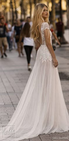 a woman in a white wedding dress standing on the sidewalk with her back to the camera