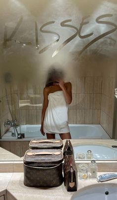 a woman standing in front of a bathroom mirror next to a bag and toiletries