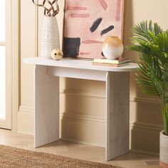 a white table with a painting on it next to a potted plant and vase