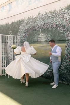 a man and woman standing next to each other near a wall with flowers on it