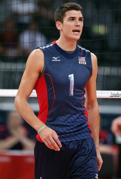 a male volleyball player is standing in front of the net with his hand on his hip