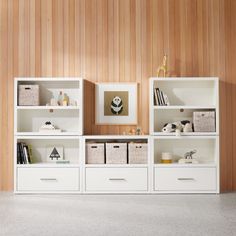 a white bookcase with baskets and books on it in front of a wooden wall